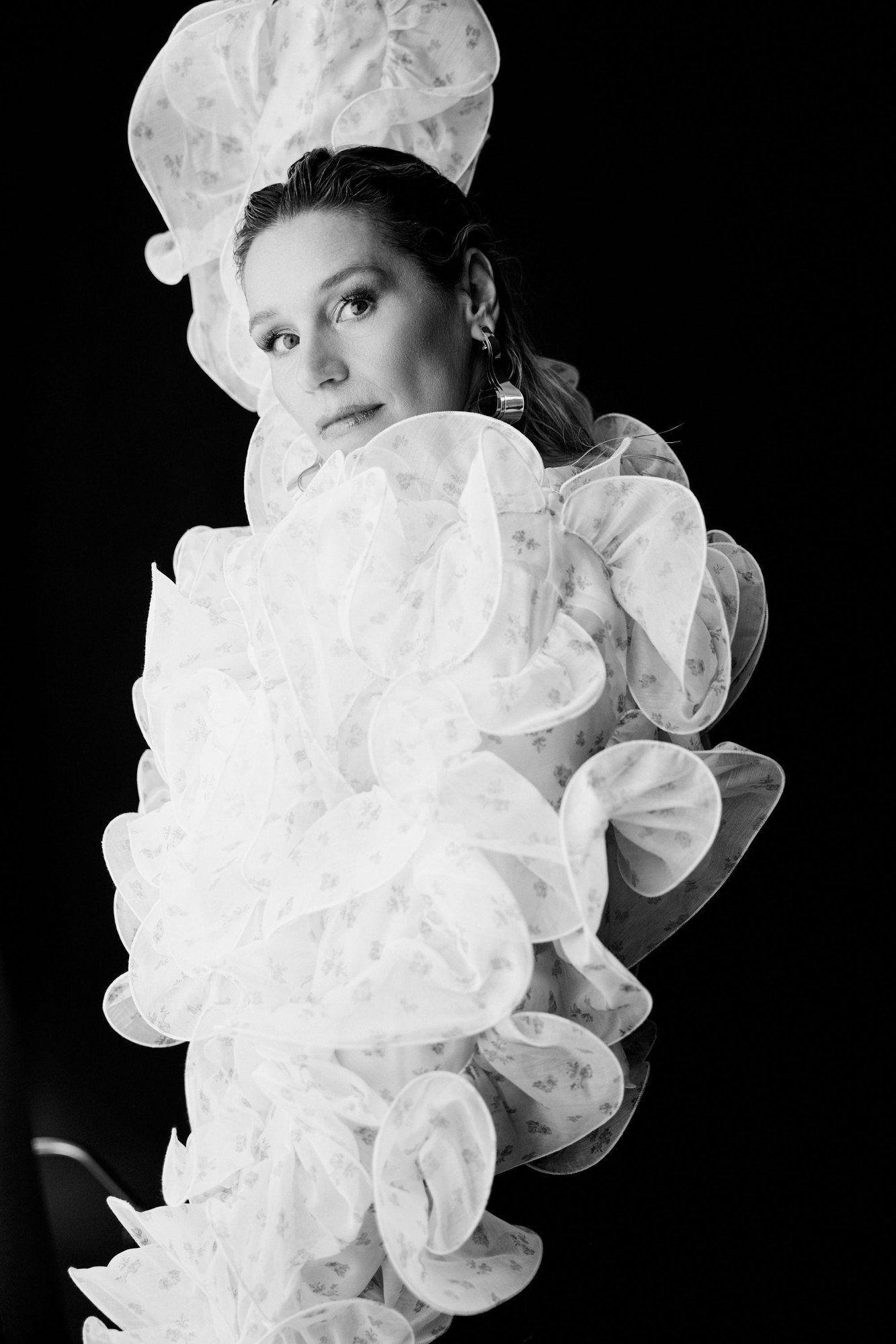 Bianca Berding, presenter, in a voluminous white ruffled dress against a black background, black and white, 2025, photographed by Kilian Amrehn