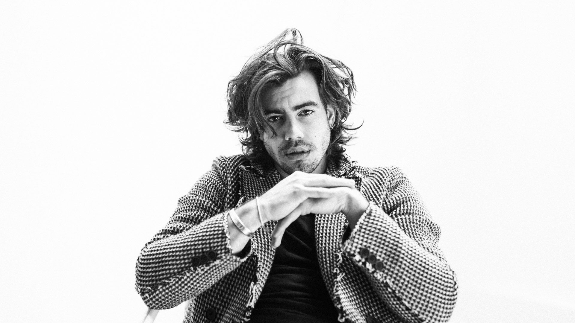Actor with wavy hair, hands clasped, tweed jacket against a white background, black and white, 2018, photographed by Kilian Amrehn