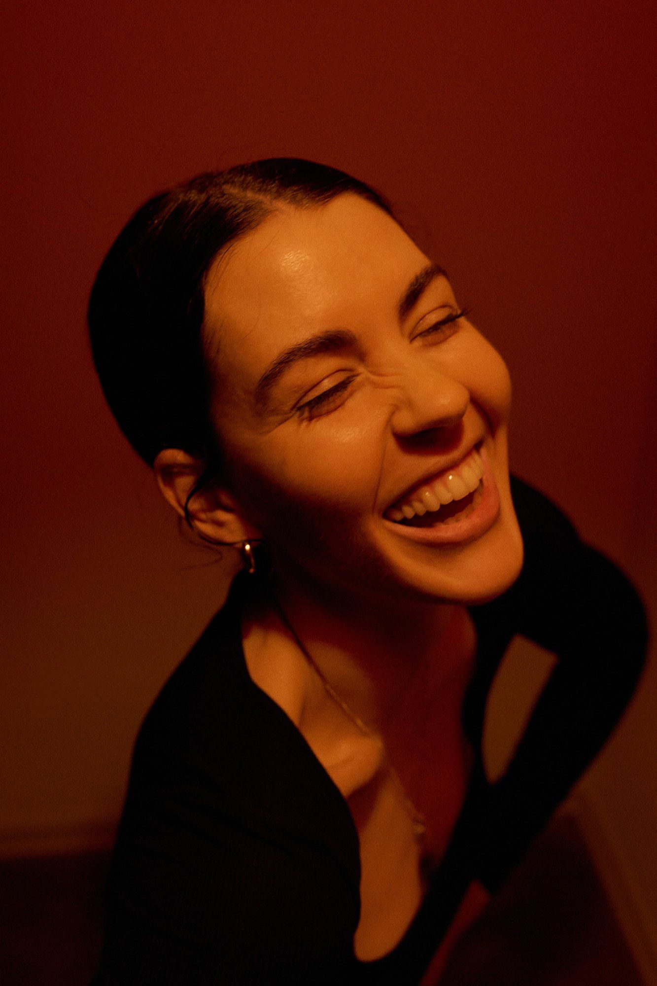 Lea Mende laughing with eyes closed in warm red light, black top, hair tied back, 2023, photographed by Kilian Amrehn
