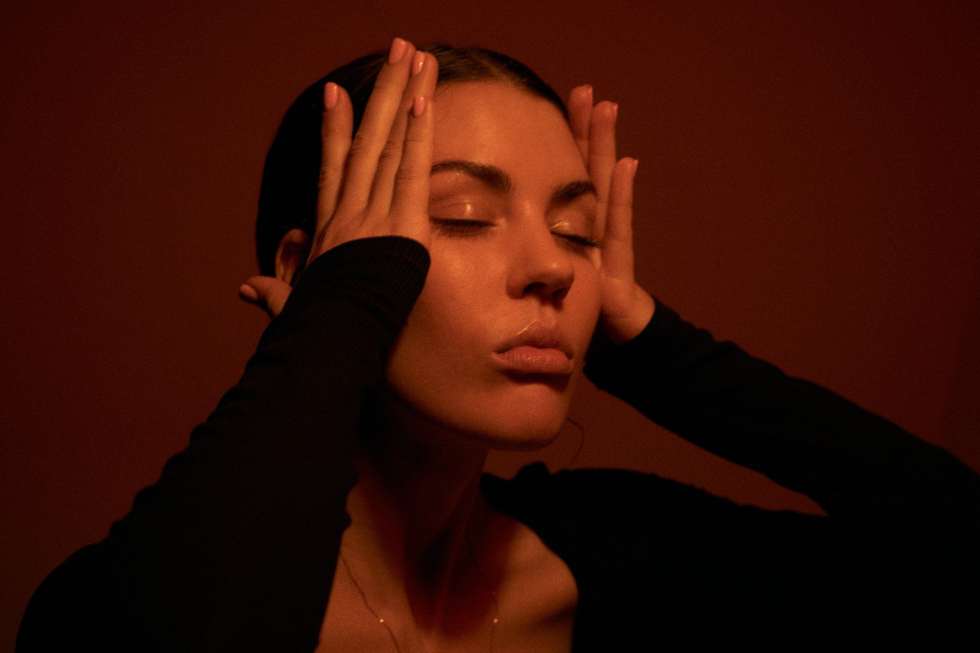 Lea Mende with eyes closed and hands at her temples, red light against a dark red wall, 2023, photographed by Kilian Amrehn