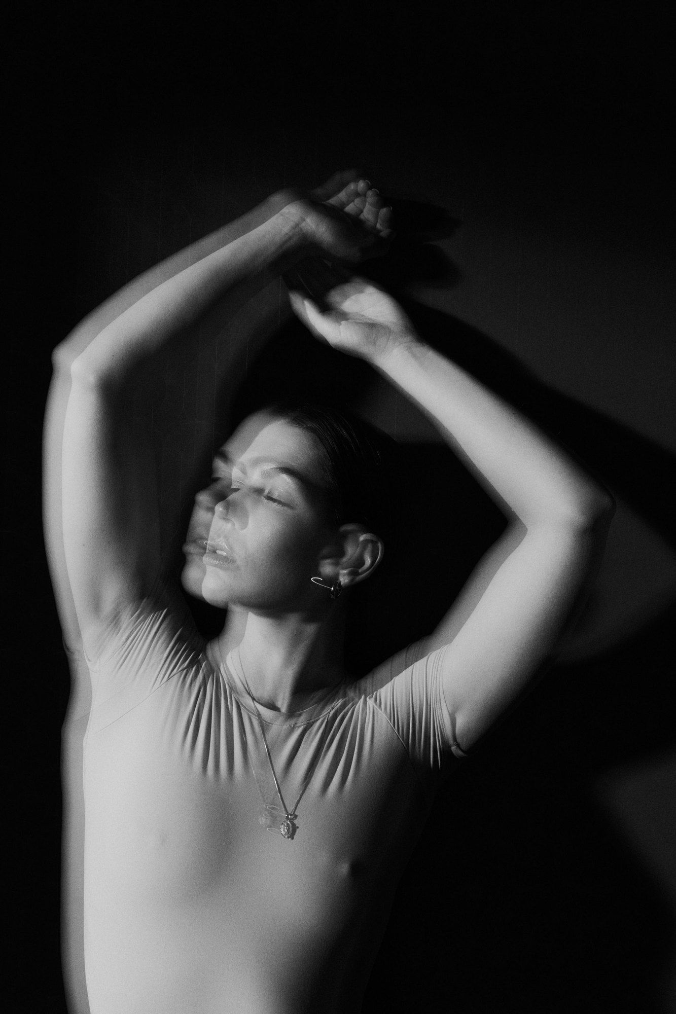 Lea Mende moving with raised arms, long exposure against a dark background, black and white, 2023, photographed by Kilian Amrehn