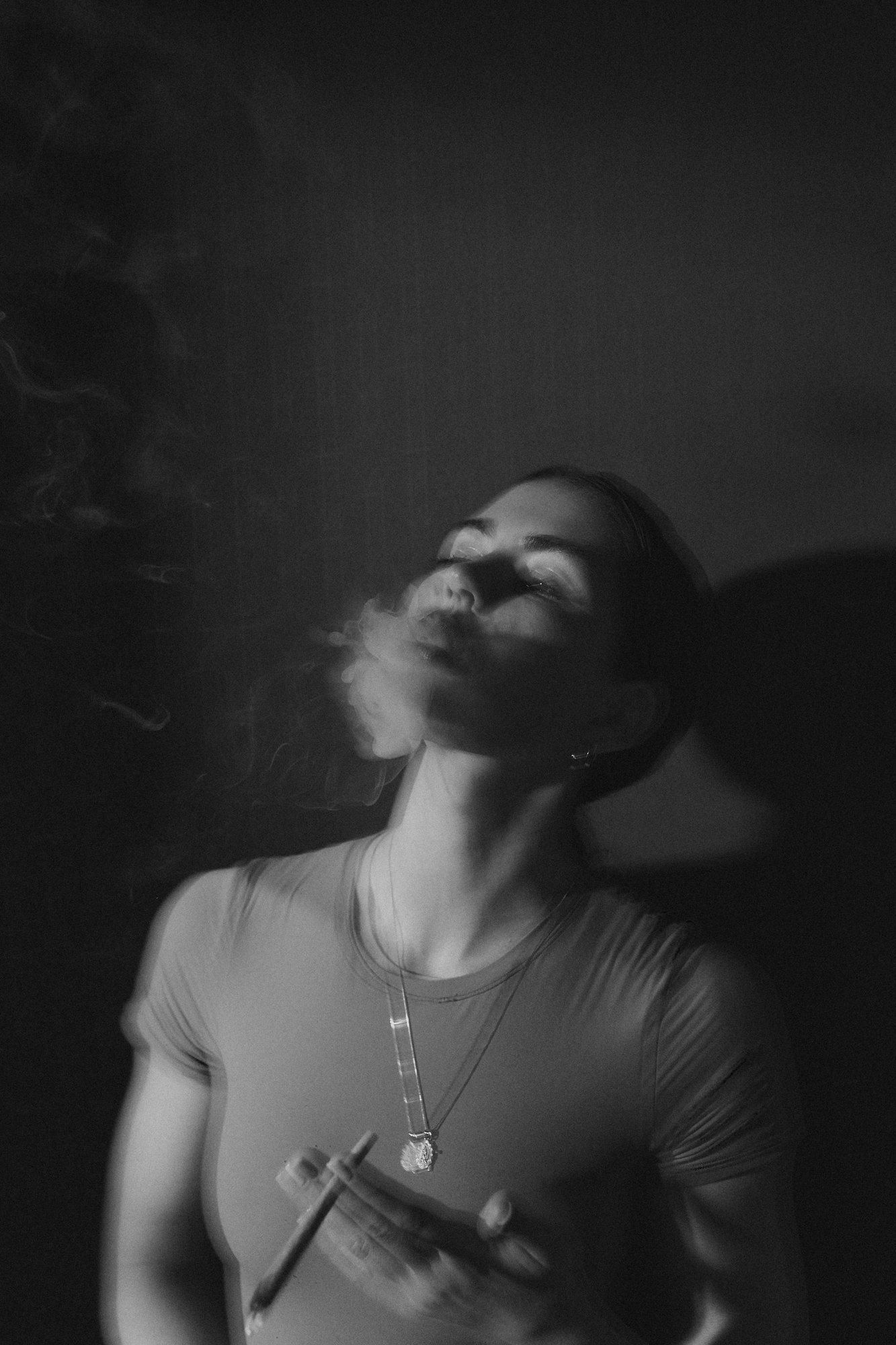 Lea Mende in a T-shirt holding a cigarette, exhaling smoke with her head tilted back, black and white in low light, 2023, photographed by Kilian Amrehn