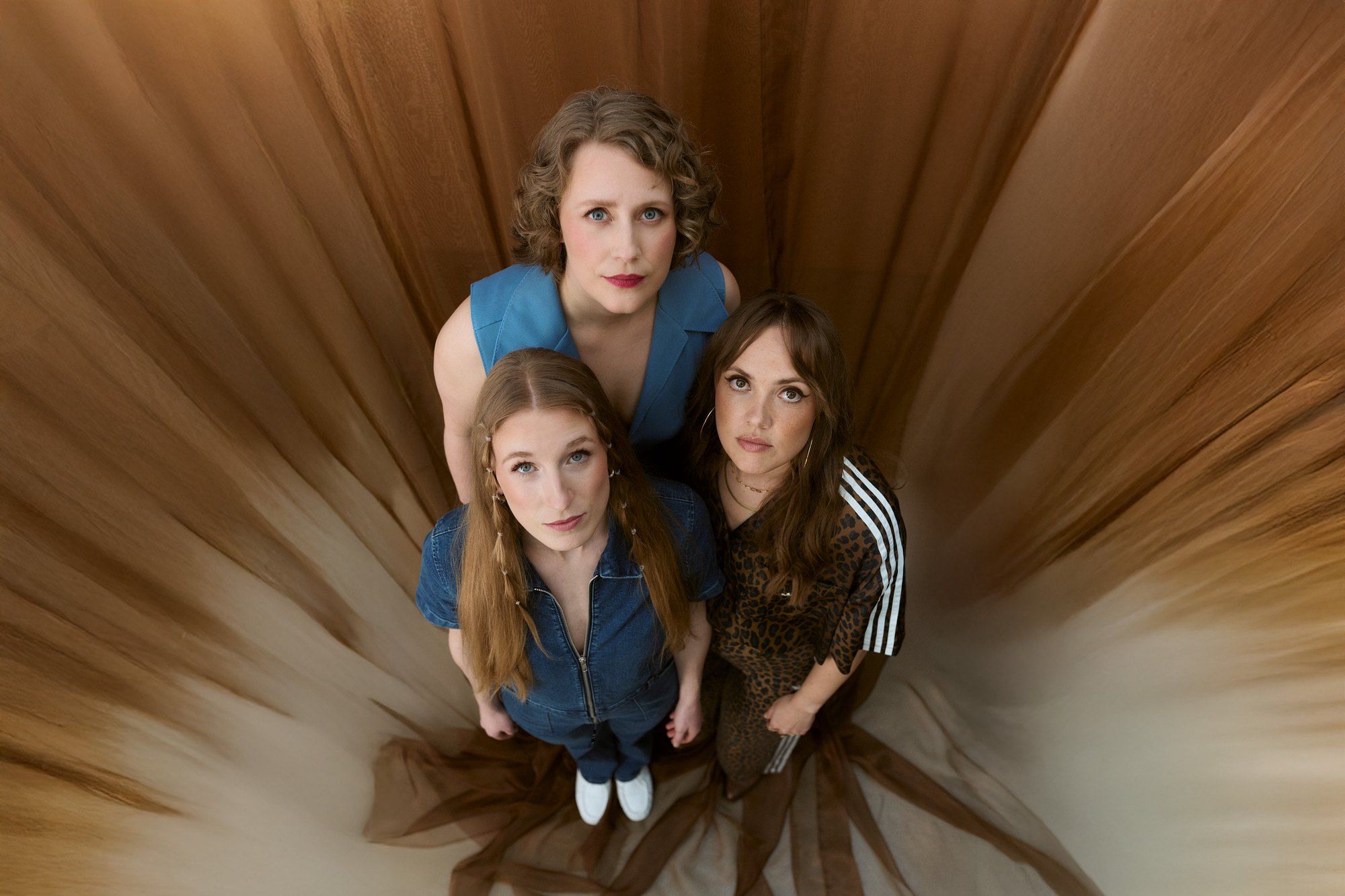 Morley, band photo, three women photographed from above amid brown tulle, denim and leopard print, 2025, photographed by Kilian Amrehn