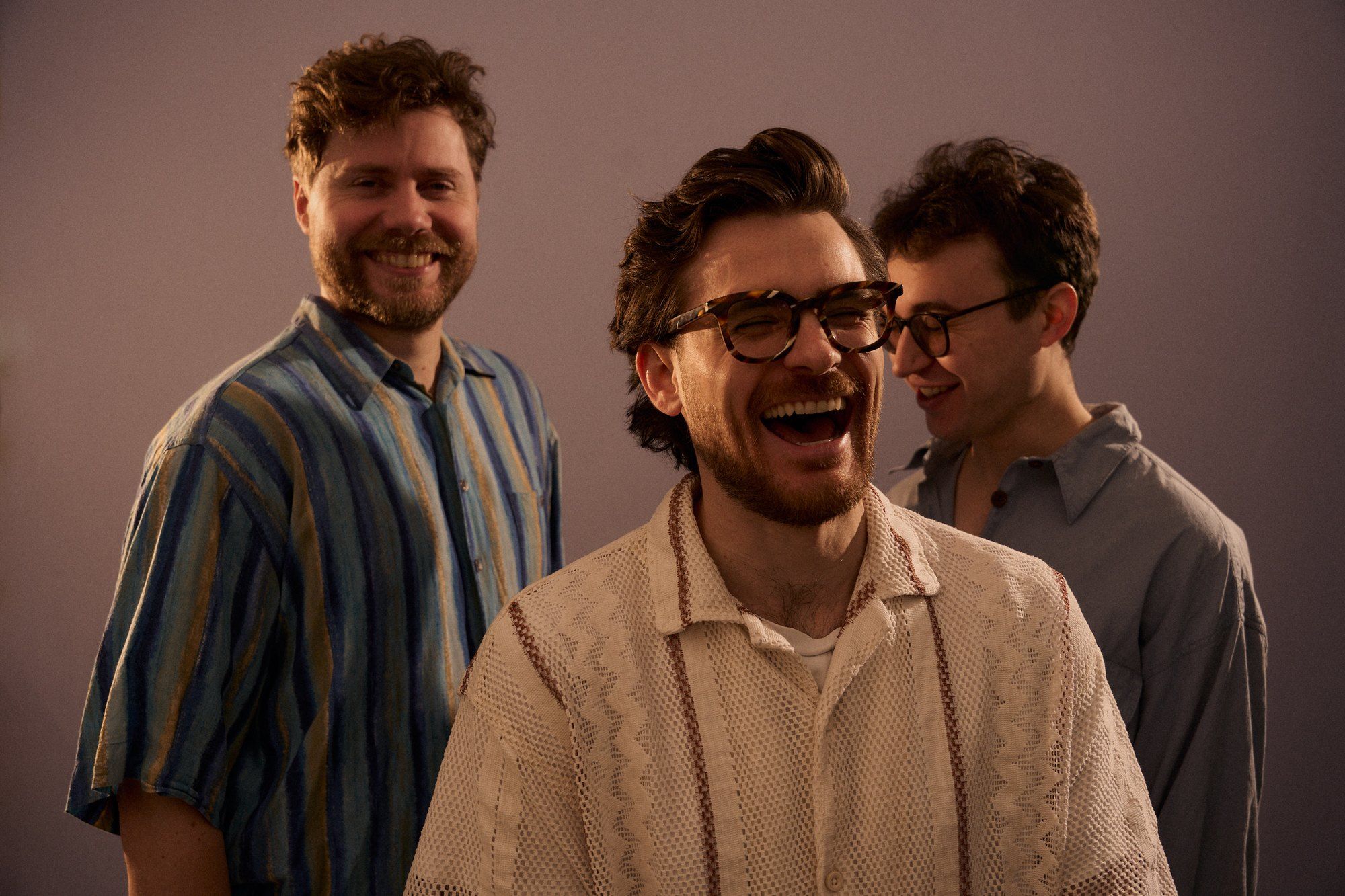 Parzhuber Trio, band photo, three musicians laughing in patterned shirts against a mauve background, 2025, photographed by Kilian Amrehn