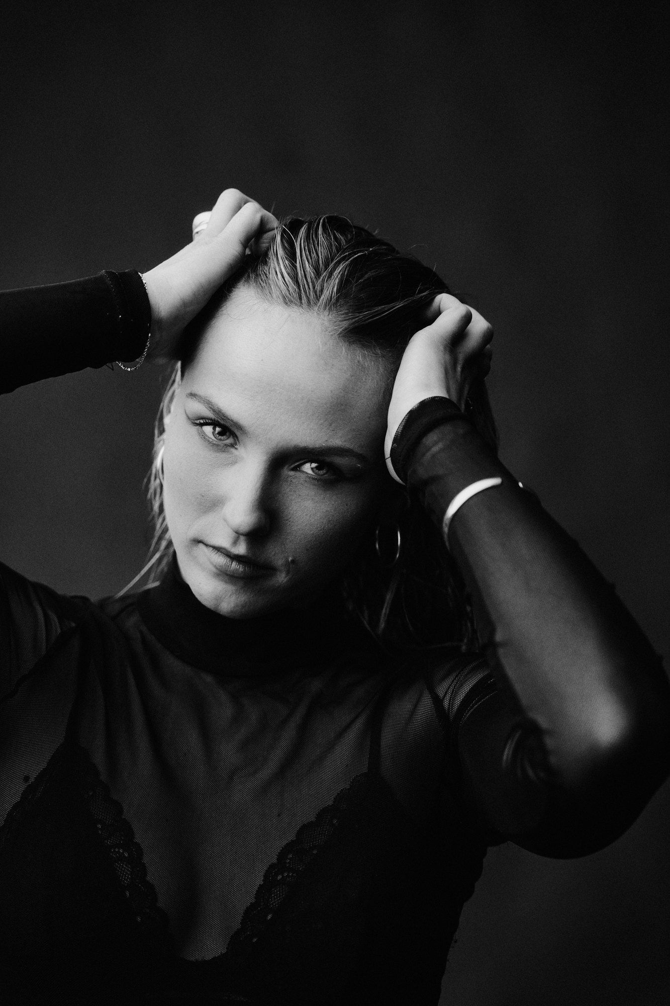 Paula, DJ, both hands in her wet hair, sheer black top, direct gaze, black and white, 2026, photographed by Kilian Amrehn