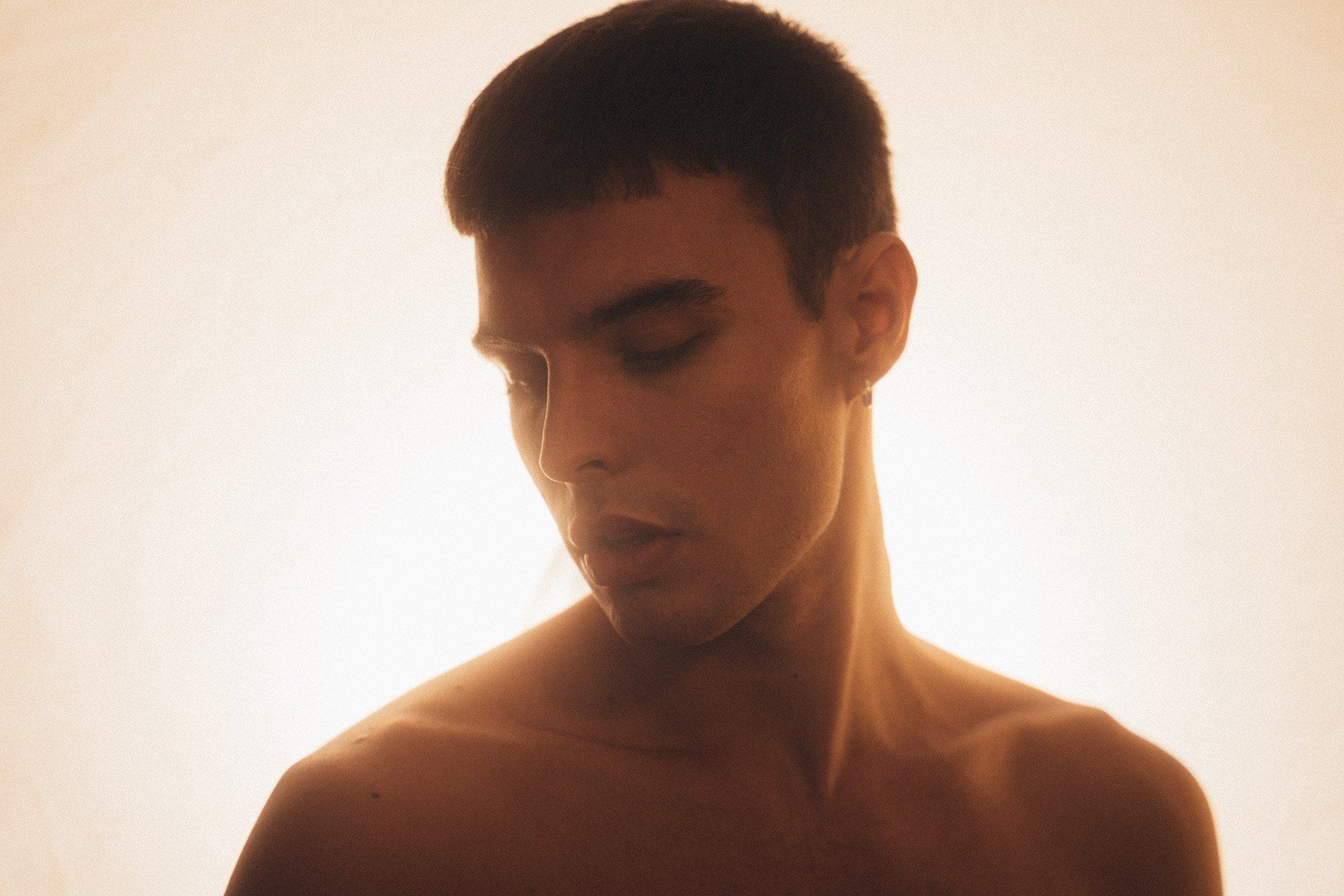 Paulus Goerden shirtless with lowered gaze in warm backlight, short dark hair, 2022, photographed by Kilian Amrehn