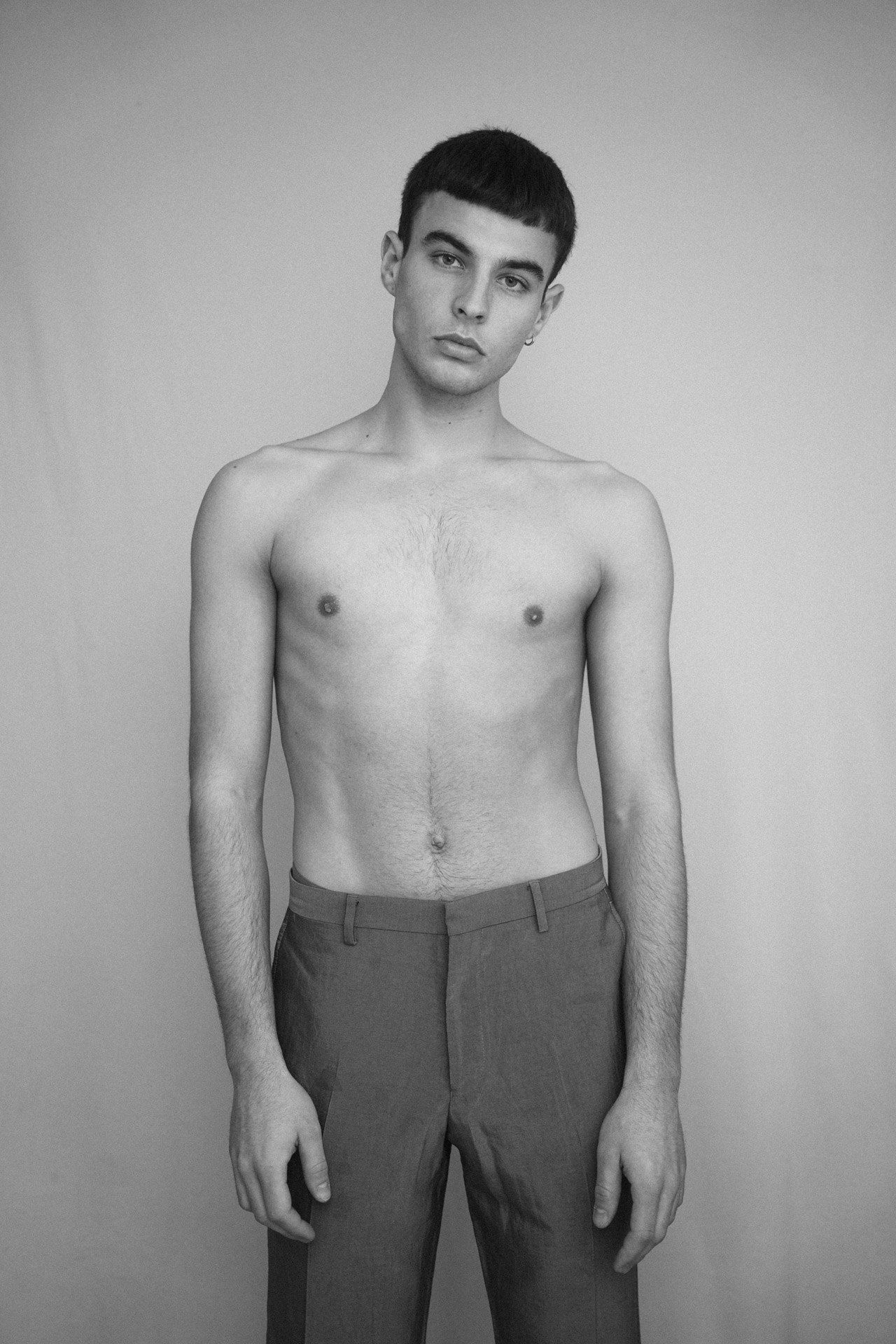 Paulus Goerden shirtless in grey trousers, standing against a light background, black and white, 2022, photographed by Kilian Amrehn
