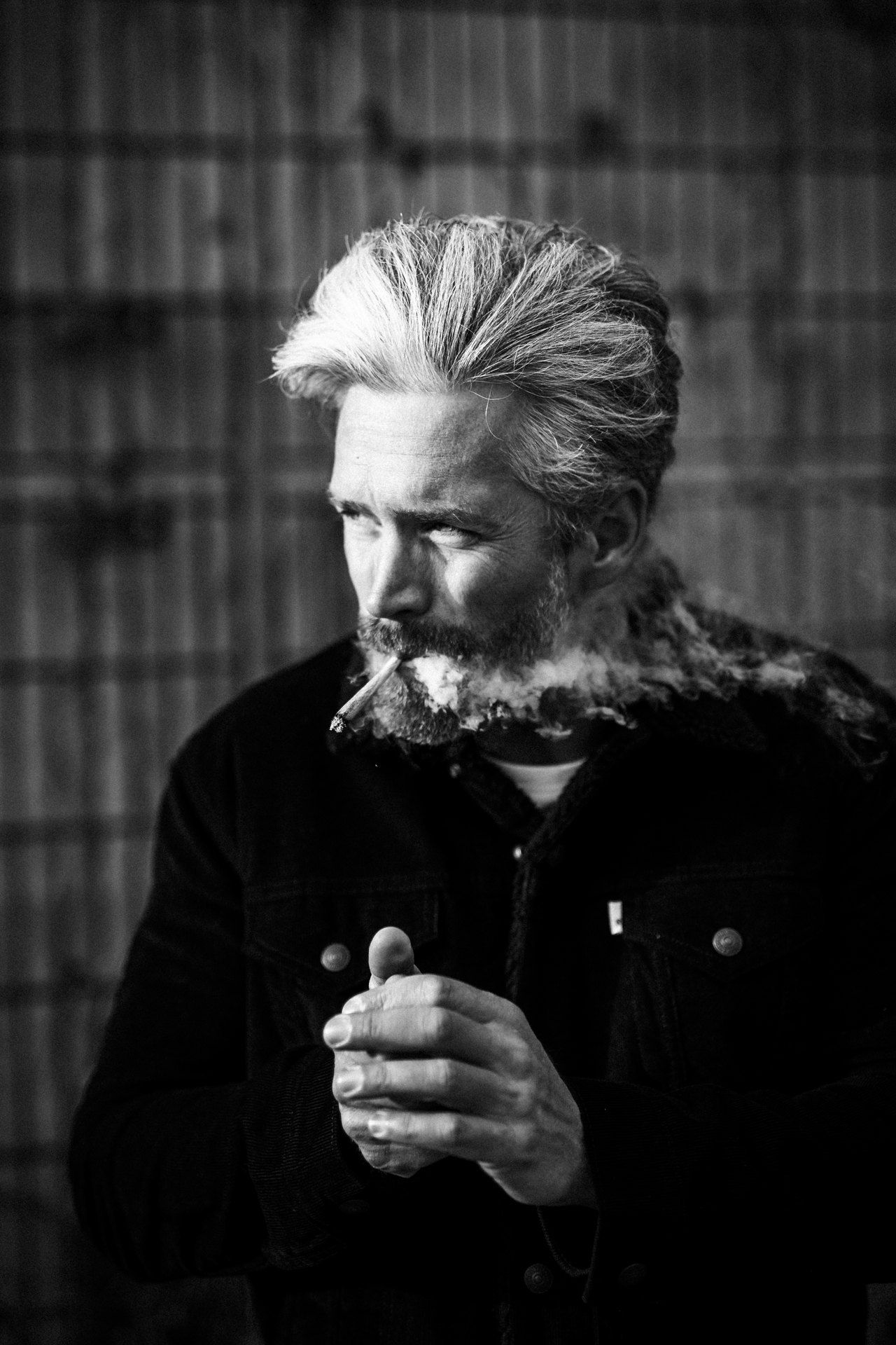 Man with grey hair and full beard, cigarette in his mouth, dark denim jacket with fur collar, black and white, 2018, photographed by Kilian Amrehn