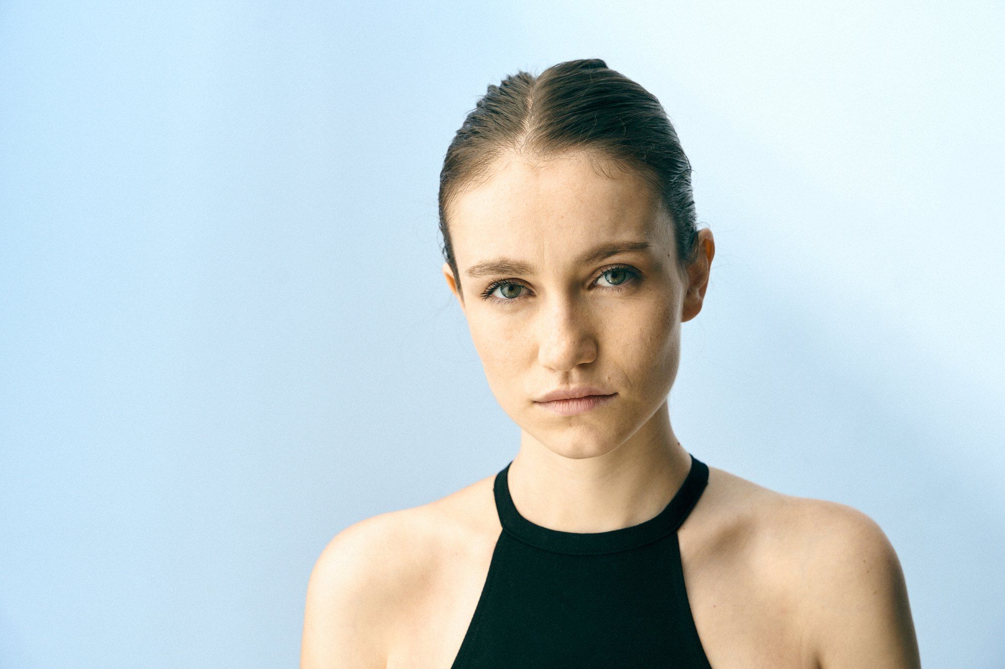 Salomé, actress, headshot with slicked-back hair and a black halter top against a light blue background, 2024, photographed by Kilian Amrehn