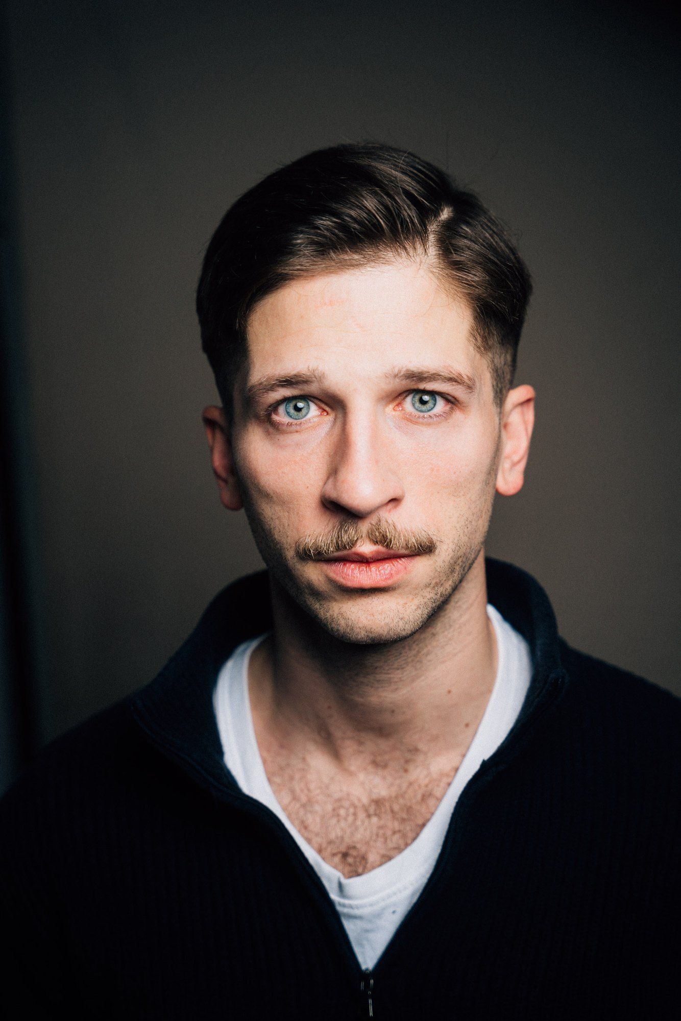 Slavko Popadić, headshot with moustache and side parting, dark sweater over a white shirt against a dark background, 2021, photographed by Kilian Amrehn