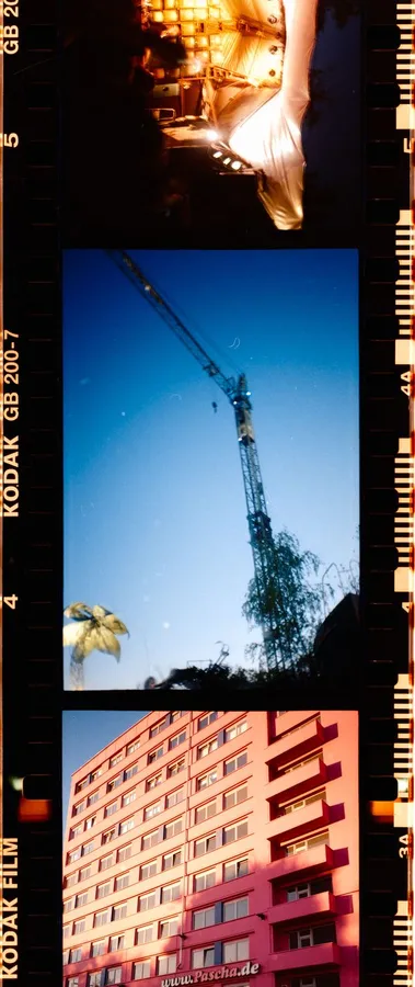 Analogue contact strip with a crane against blue sky, a palm tree and a red high-rise, flash by Kilian Amrehn