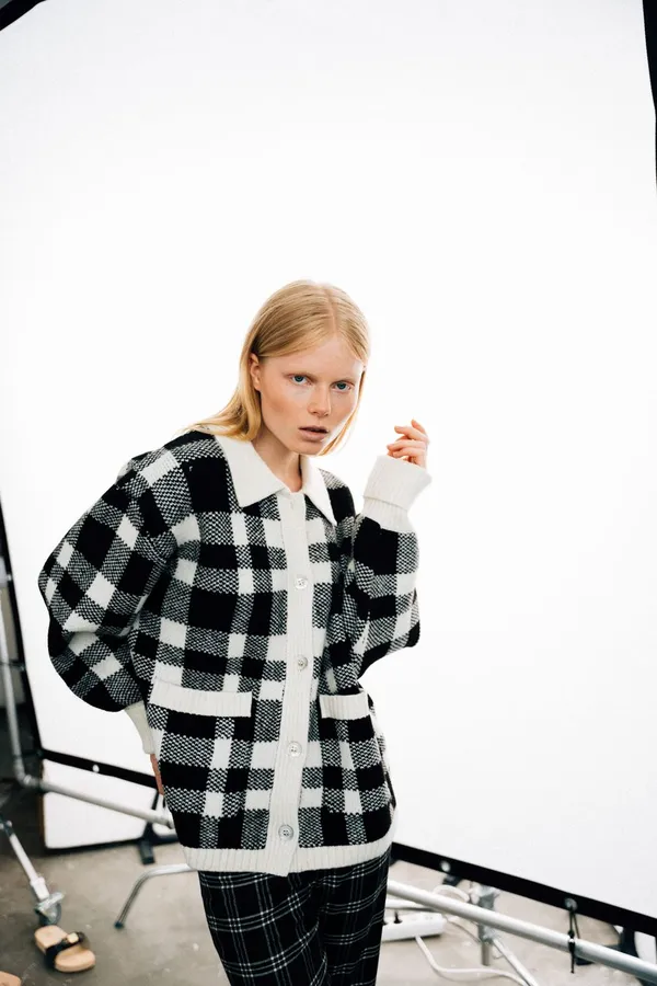 Blonde woman in a black and white checked knit cardigan against a white studio backdrop, flash by Kilian Amrehn