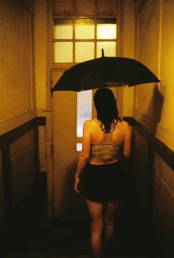 Woman with an umbrella seen from behind in a warmly lit hallway, analogue, flash by Kilian Amrehn