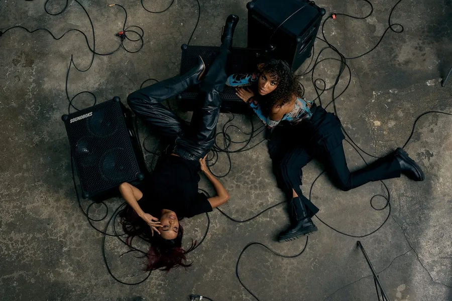 Two women lie among speaker boxes and cables on a concrete floor, analogue, flash by Kilian Amrehn