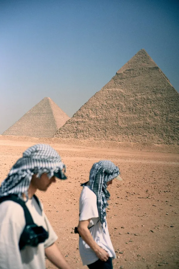 Two men in checked headscarves walk towards the Pyramids of Giza, flash by Kilian Amrehn