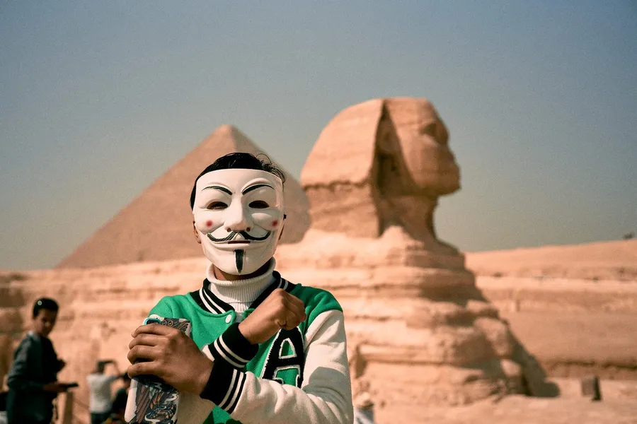Man in a Guy Fawkes mask and varsity jacket before the Sphinx and pyramid, Giza, flash by Kilian Amrehn