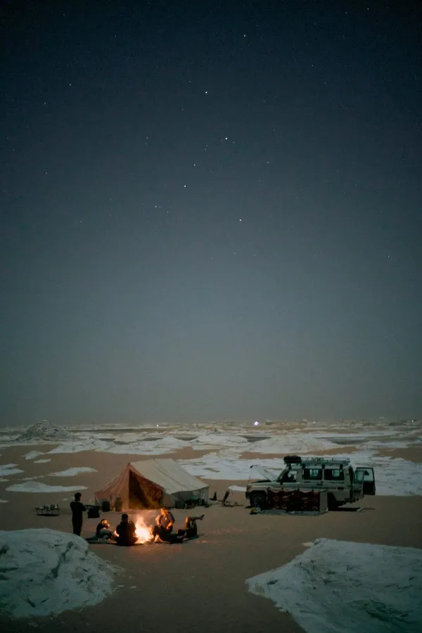Night camp with campfire, tent and off-road car under a starry desert sky, flash by Kilian Amrehn