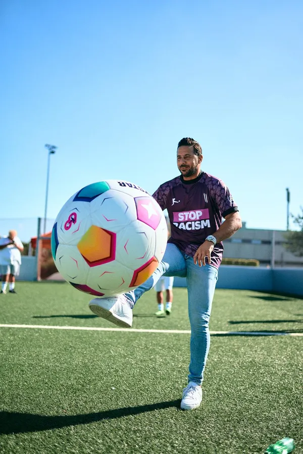 Man in a Stop Racism jersey juggles a colourful ball on an artificial pitch, flash by Kilian Amrehn