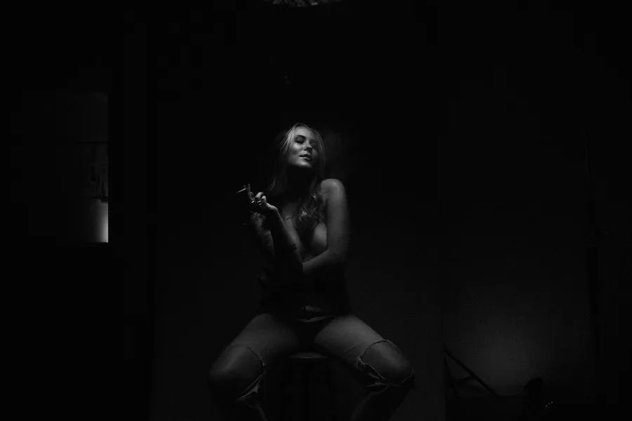 Woman with a cigarette sits in an almost dark room, faintly lit, flash by Kilian Amrehn