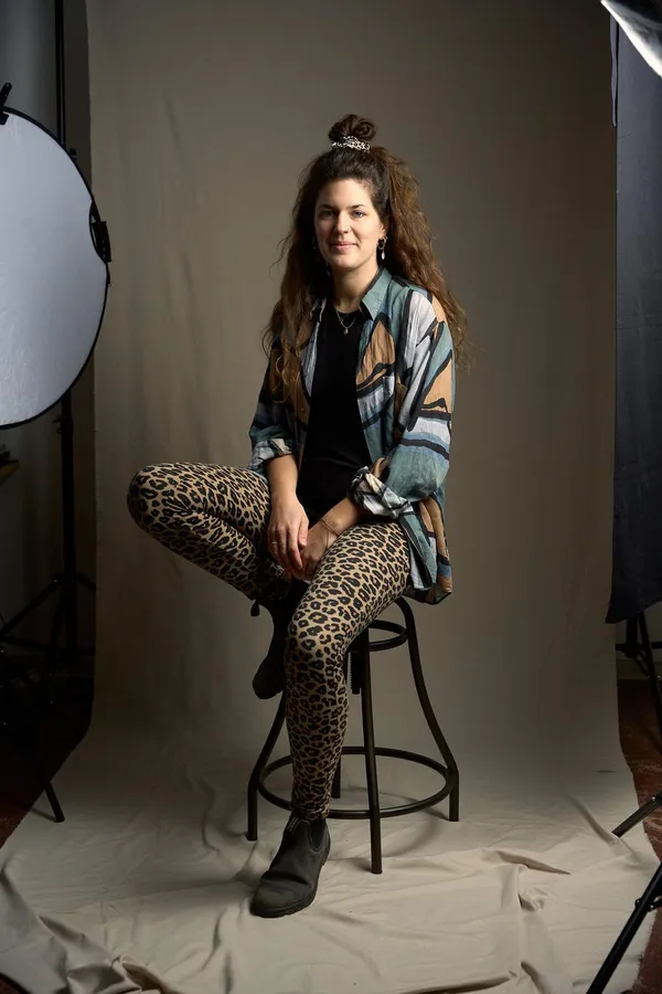 Woman in leopard leggings sits on a bar stool before a studio backdrop with lights, flash by Kilian Amrehn