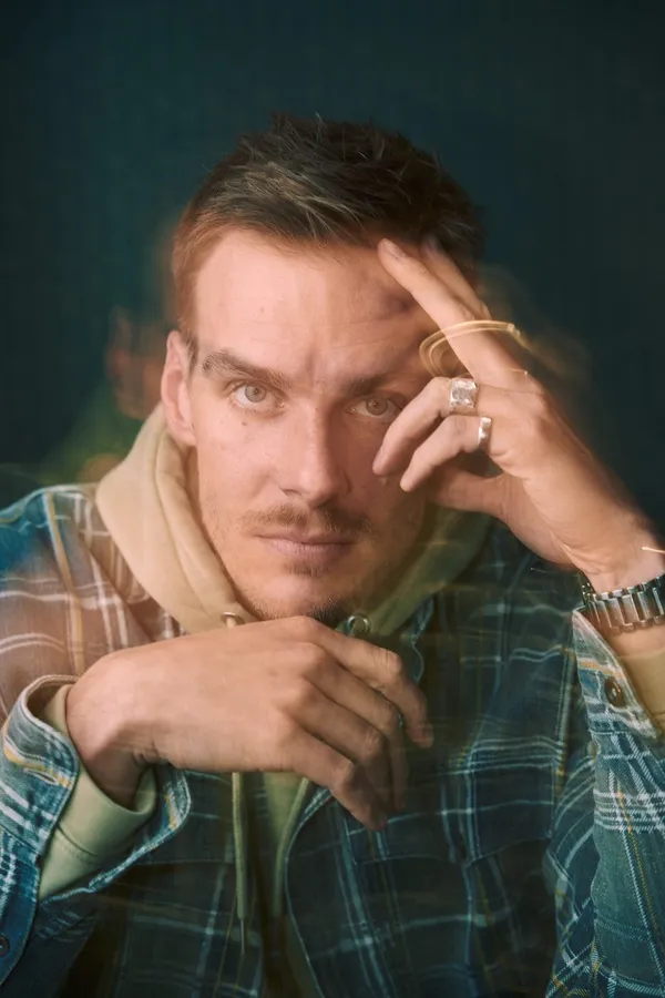 Man with a moustache and rings rests his head in his hand, green background, flash by Kilian Amrehn
