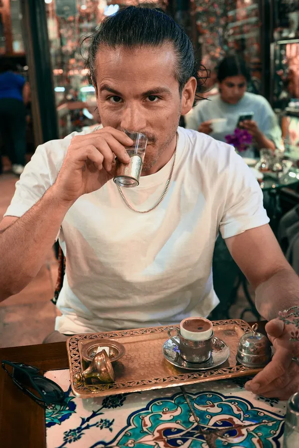 Man sips coffee from a small glass at a table with a copper tray and mosaic top, flash by Kilian Amrehn