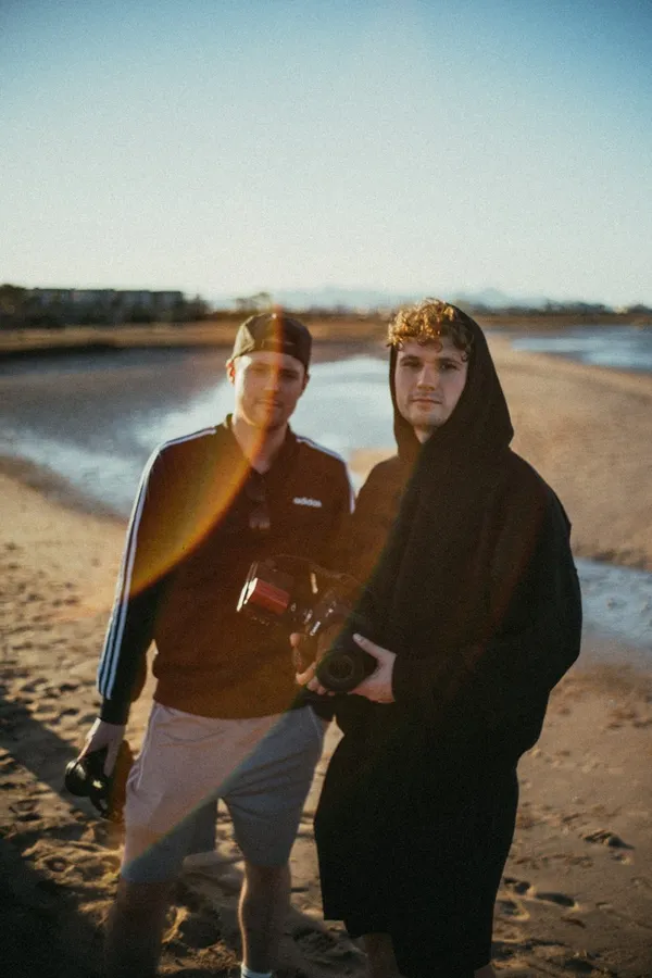 Two young men with cameras on a beach backlit by the low sun, flash by Kilian Amrehn