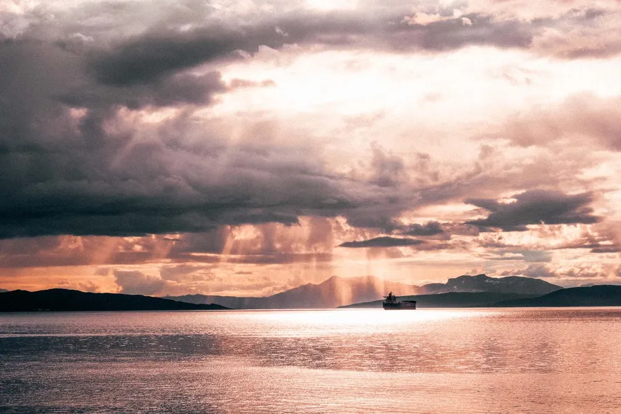 Dramatic cloudy sky with sunbeams over the sea, mountains and a ship, flash by Kilian Amrehn