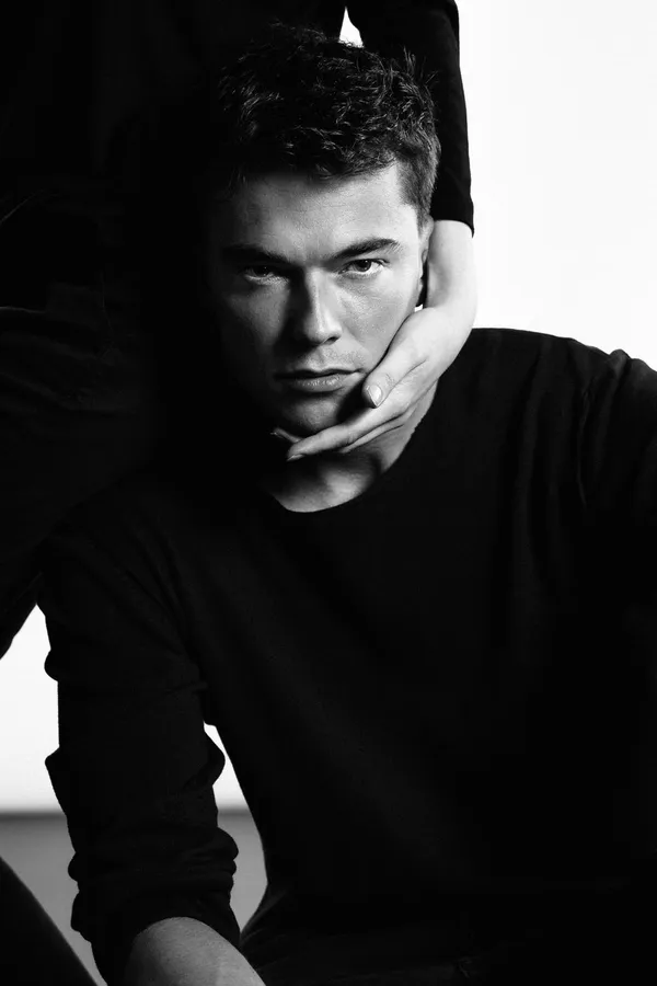 Young man in a black sweater, another person's hands cradle his chin, black and white, flash by Kilian Amrehn