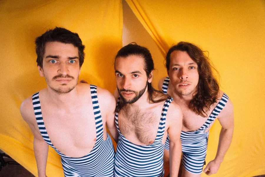 Three men in striped retro bathing suits in front of yellow fabric, flash by Kilian Amrehn