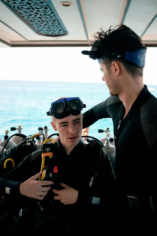 Two young divers in wetsuits with masks on their heads on a boat, flash by Kilian Amrehn