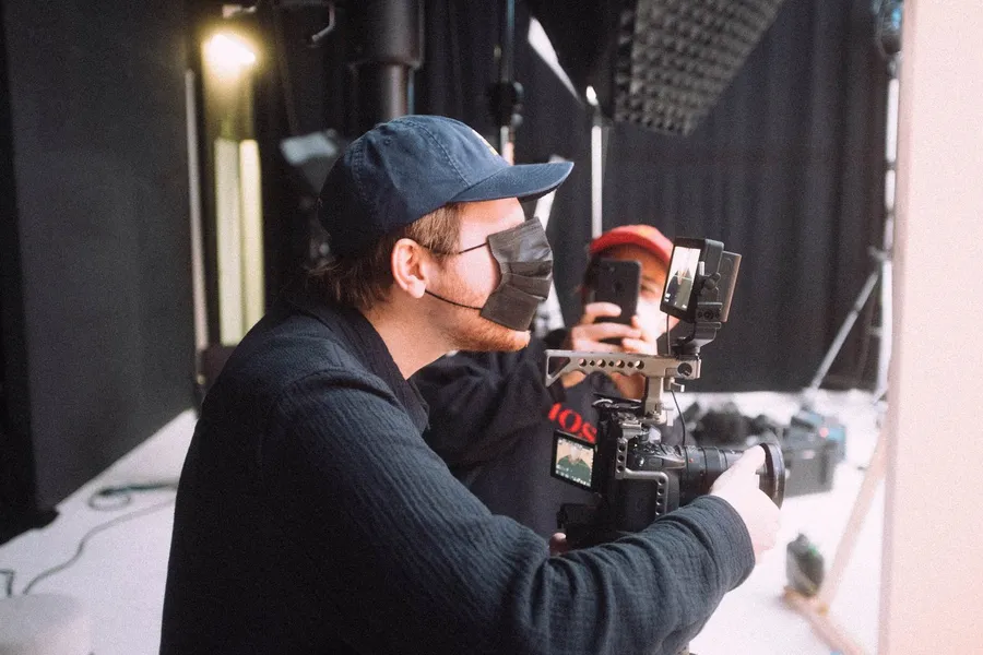 Cameraman in a mask and cap with a gimbal, backstage at a studio video shoot, flash by Kilian Amrehn