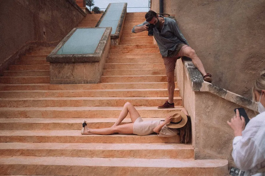 Photographer on sunny stone steps shoots a reclining model with a straw hat, flash by Kilian Amrehn