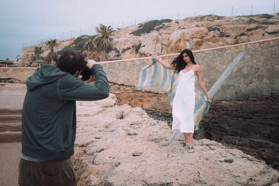 Photographer shoots a woman in a white dress with a scarf on coastal rocks, flash by Kilian Amrehn