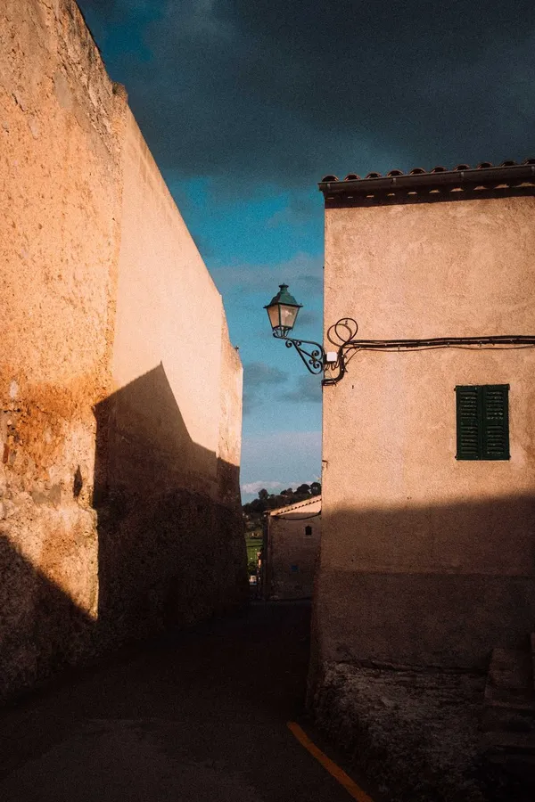 Narrow alley with ochre walls and a street lamp in evening light, blue sky, flash by Kilian Amrehn