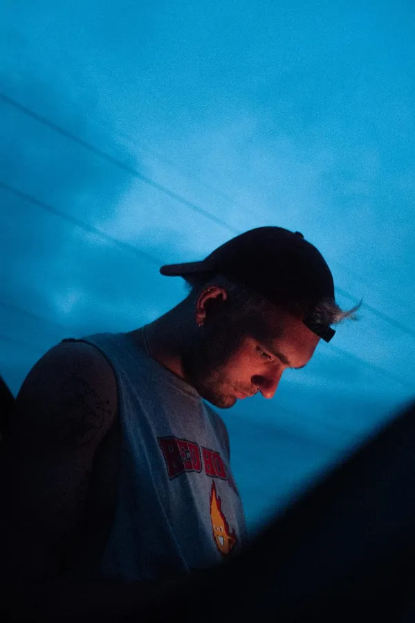 Man in a cap with a headlamp looks down against a deep blue sky, flash by Kilian Amrehn