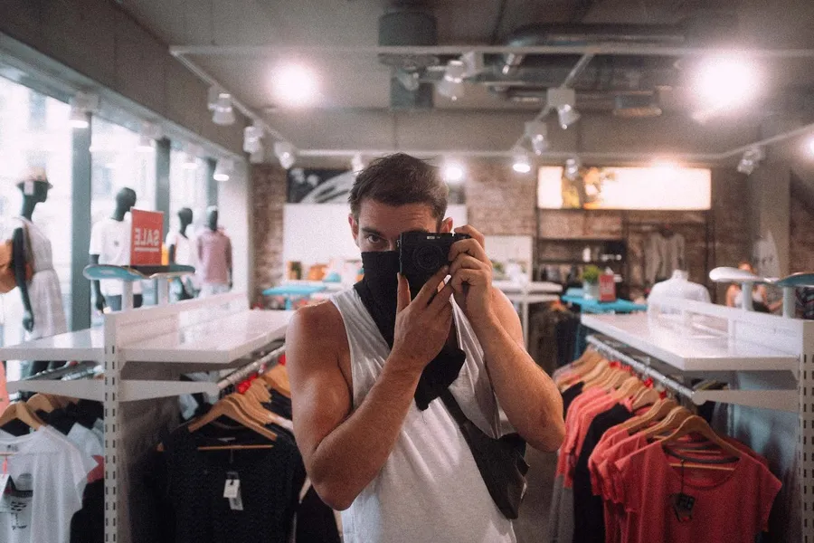 Mirror selfie of a man with a camera and neckerchief in a clothing store, flash by Kilian Amrehn