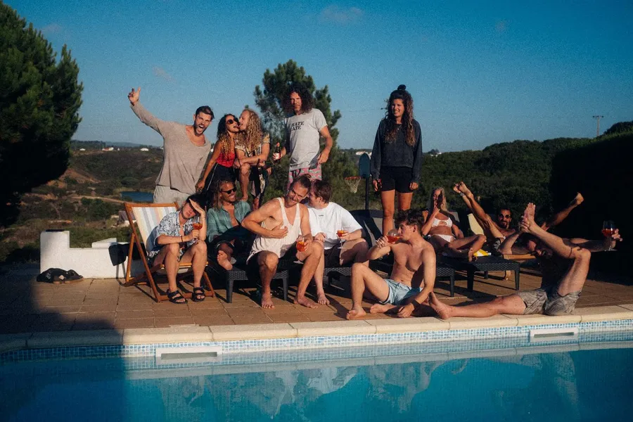 Exuberant group of friends by a pool with loungers under a blue sky, flash by Kilian Amrehn