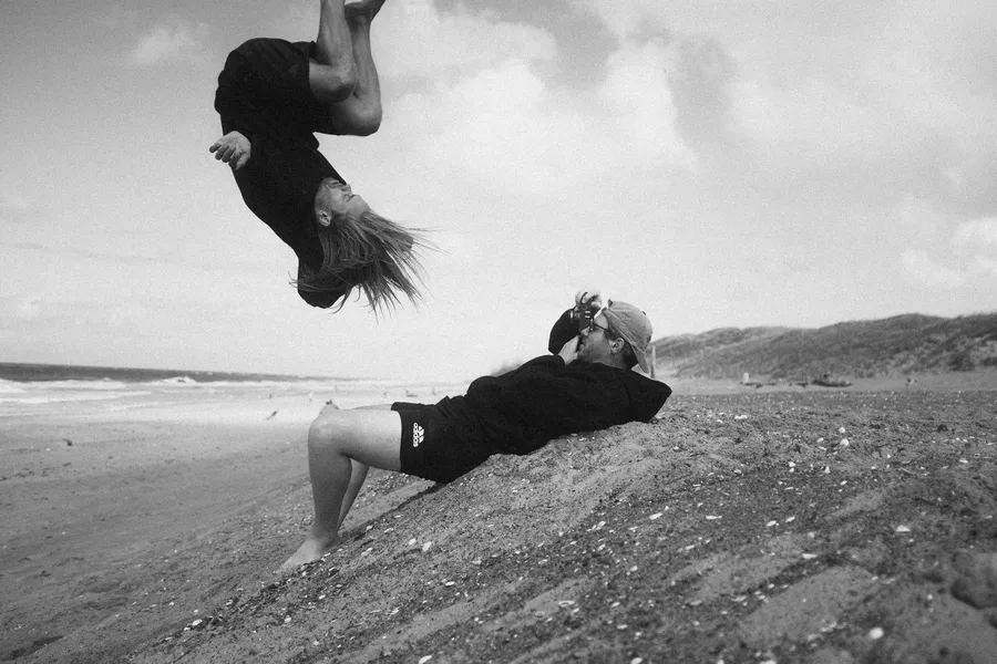 Man does a backflip over a reclining friend on the beach, black and white, Denmark, flash by Kilian Amrehn