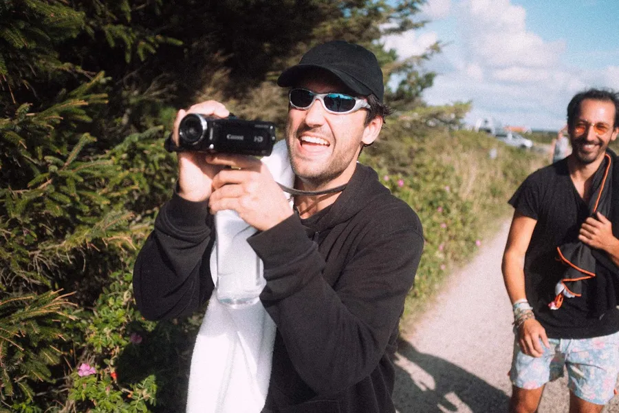 Laughing man films with a camcorder on a hedge-lined path, friend behind, Denmark, flash by Kilian Amrehn