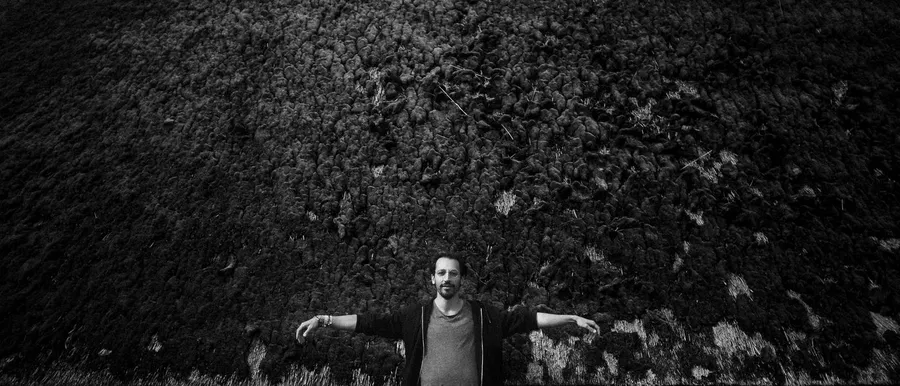 Man with outstretched arms before a dark overgrown wall, black and white, Denmark, flash by Kilian Amrehn