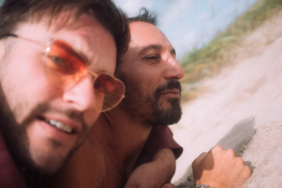 Two men in the sand, one in heart-shaped sunglasses, selfie close-up, Denmark, flash by Kilian Amrehn