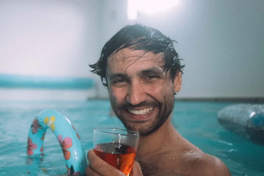 Laughing man holding rosé in a pool with an inflatable ring, Denmark, flash by Kilian Amrehn