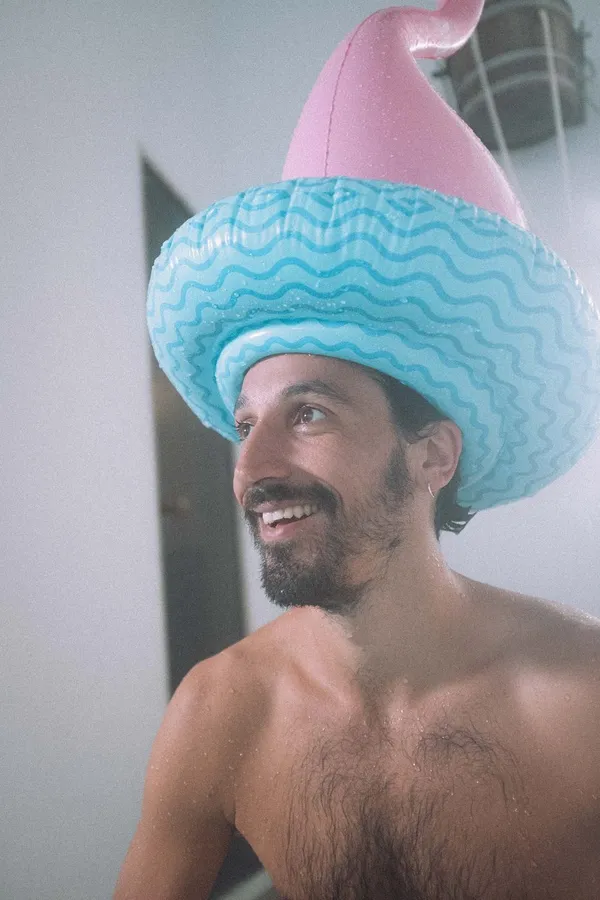 Laughing shirtless man in a turquoise and pink inflatable hat, Denmark, flash by Kilian Amrehn