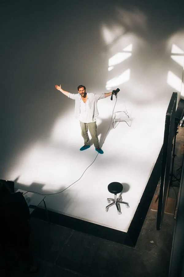 Man with arms spread in a bright pool of light on a white studio floor, Denmark, flash by Kilian Amrehn