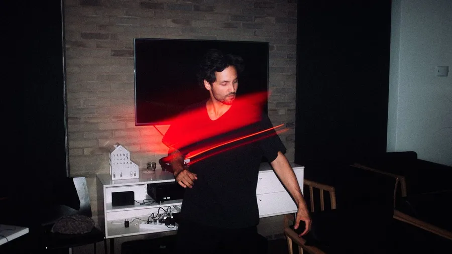 Man dances in a living room at night, red light trails from long exposure, Denmark, flash by Kilian Amrehn