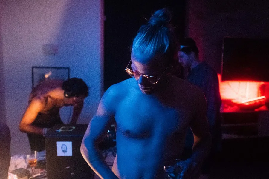 Man with a bun and glasses in blue and red light at a house party, Denmark, flash by Kilian Amrehn