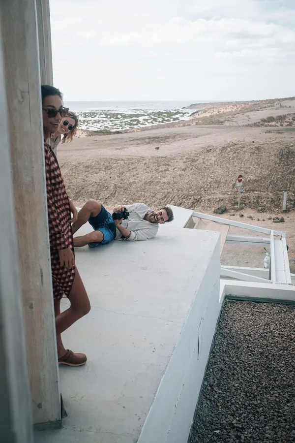 Friends lie and lean on a white flat roof above a barren coastal landscape, Denmark, flash by Kilian Amrehn