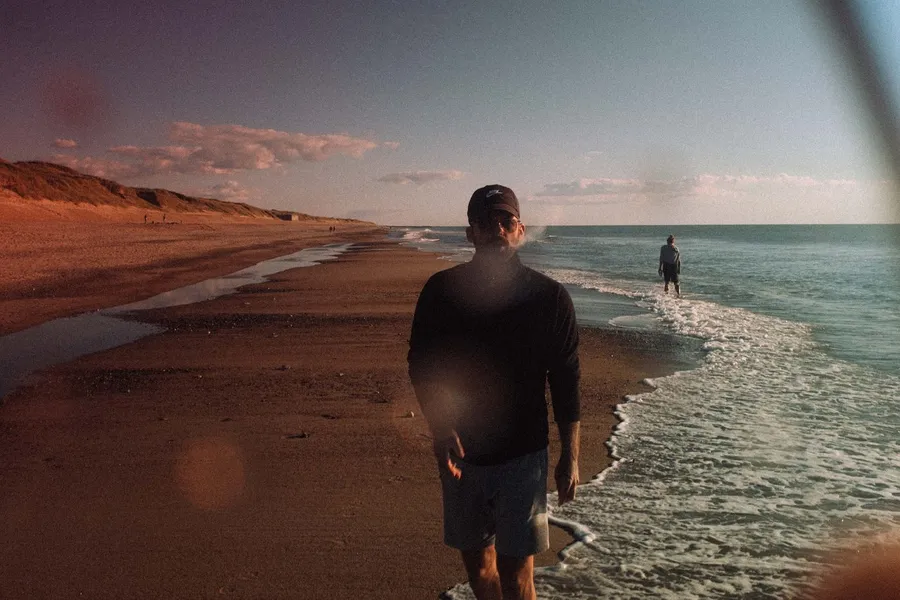 Man on a beach in low evening sun with waves and dunes, lens flares in frame, Denmark, flash by Kilian Amrehn