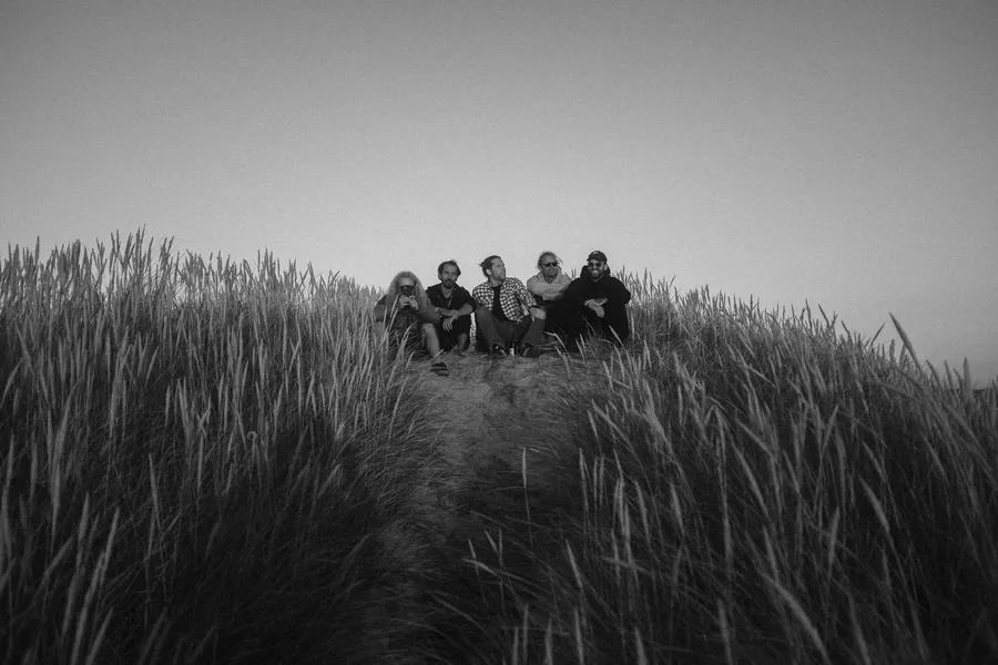 Five friends sit on a dune behind tall marram grass, black and white, Denmark, flash by Kilian Amrehn